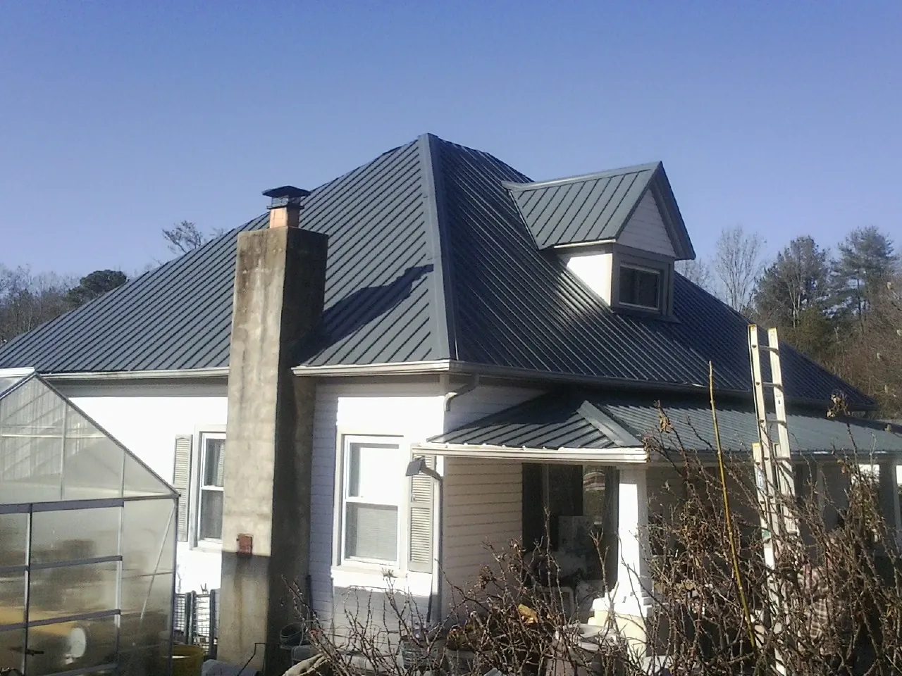 Dark blue standing seam metal roof on a white farmhouse with dormer — Slate & Tile Roof Repair by Roofing Brothers in Oketo