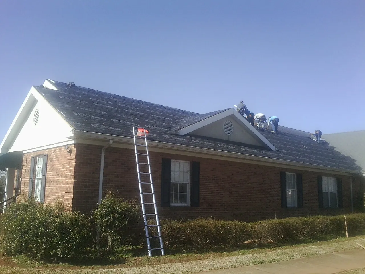Crew tearing shingles off a brick ranch roof with a ladder set — Metal Roof Repair work by our crew in Oketo