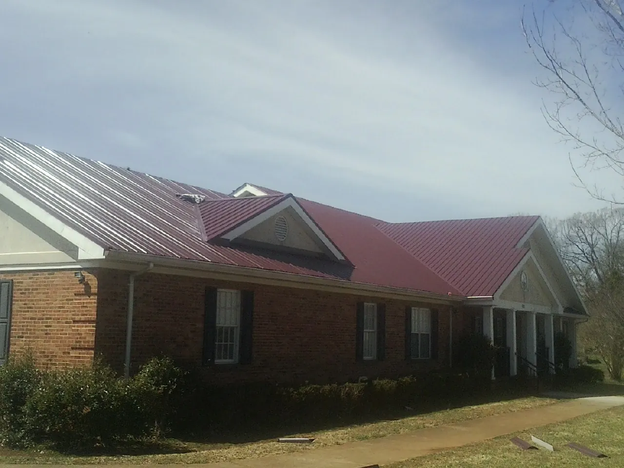 Red metal roof with gabled entries on a long brick building, from a Hail Damage Roof Repair job in Oketo