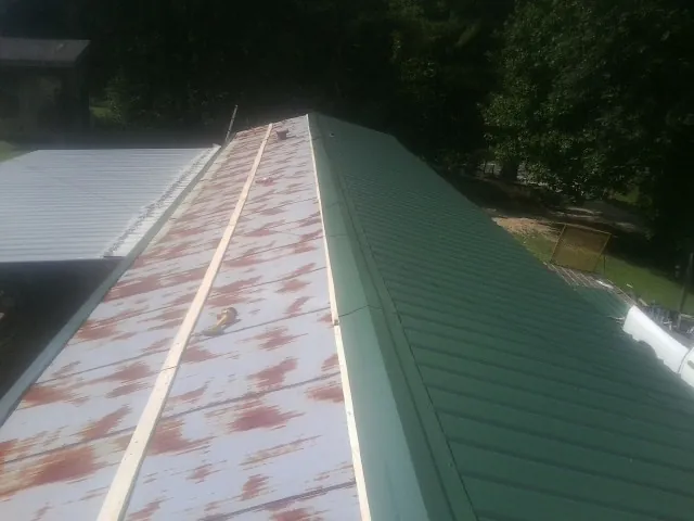 Old rusted panels beside newly installed green metal roofing — Wind Damage Roof Repair by Roofing Brothers in Oketo