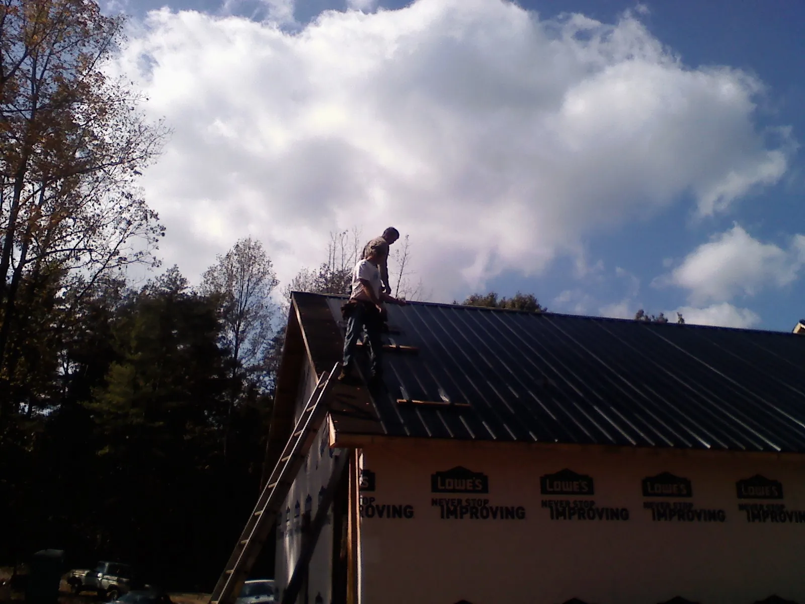 Roofer fastening dark metal panels high against a cloudy sky, from a Roof Inspection job in Oketo