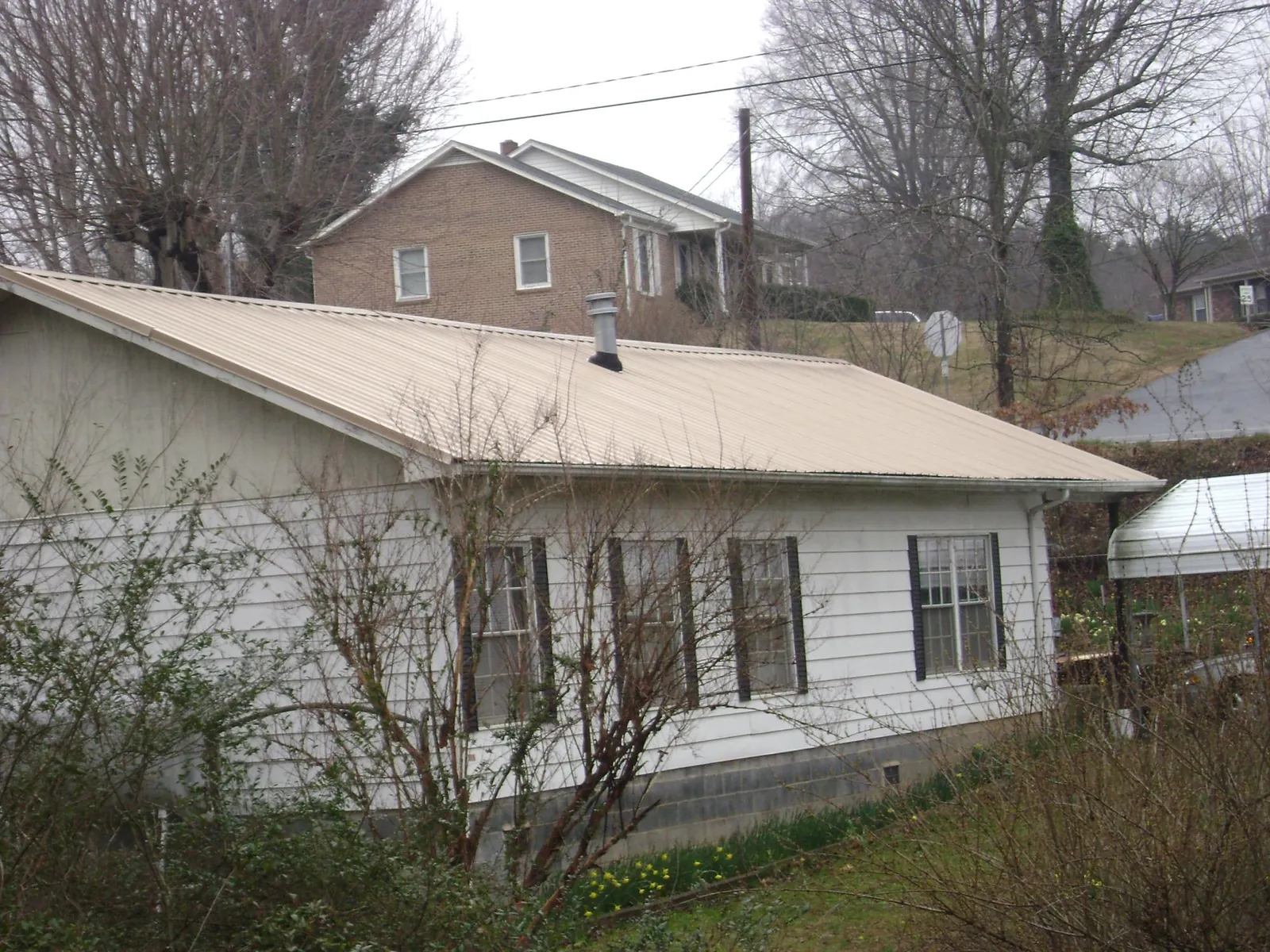 Tan metal roof on a white sided house set into a hillside — Commercial Roofing by Roofing Brothers in Oketo