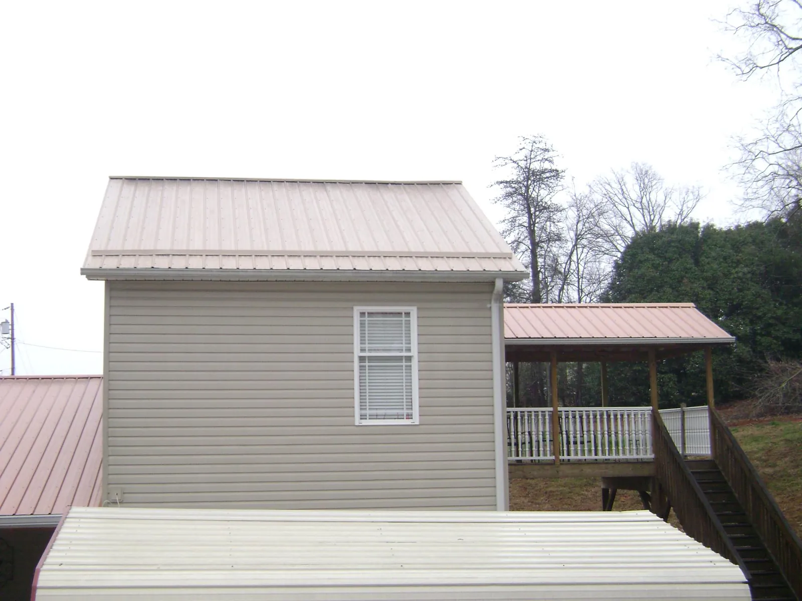Tan metal roofs on a two story addition and attached porch, from a Roof Replacement job in Oketo